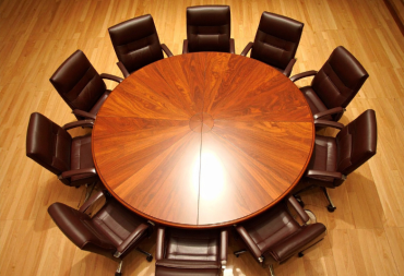 Grande table ronde en bois entourée de fauteuils de réunion en cuir, vue de dessus.