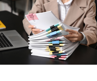 Personne consultant une pile de dossiers et documents sur un bureau