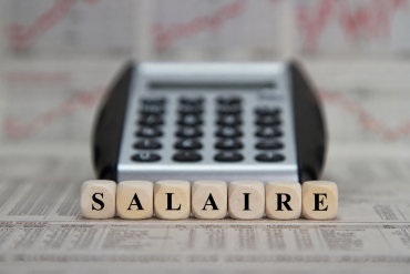 Cubes en bois formant le mot « SALAIRE » devant une calculatrice et des documents financiers.